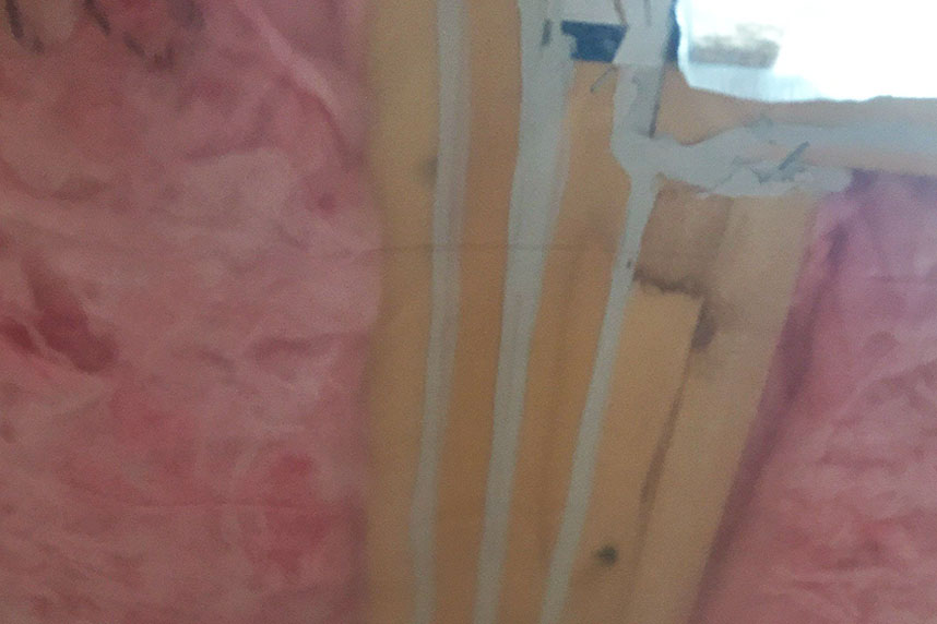 Close-up of pink fiberglass insulation with spray foam air sealing around electrical wire penetration in a wood-framed wall.