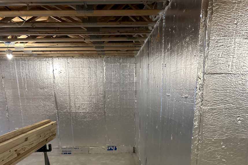 Interior basement walls lined with reflective rigid foam insulation panels, with exposed floor joists overhead