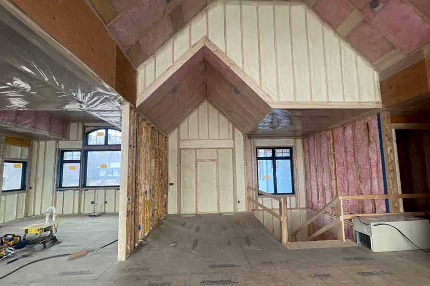 Residential attic undergoing spray foam insulation installation, walls covered, windows visible