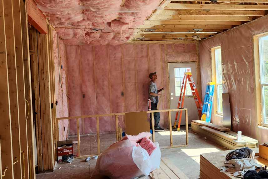 Cullen Insulation technician installing vapor barrier plastic sheeting over fiberglass batt insulation inside a residential building under construction.