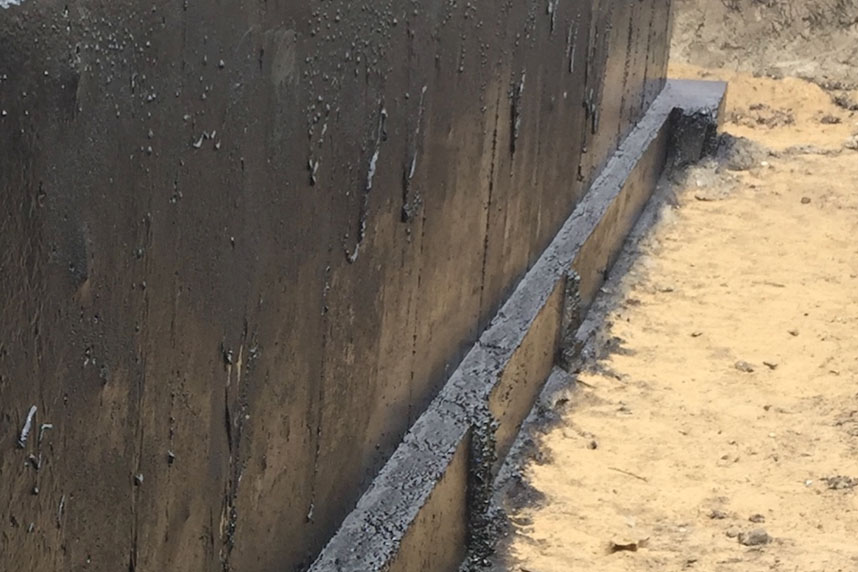 Residential foundation wall coated in black tar for waterproofing and moisture control.