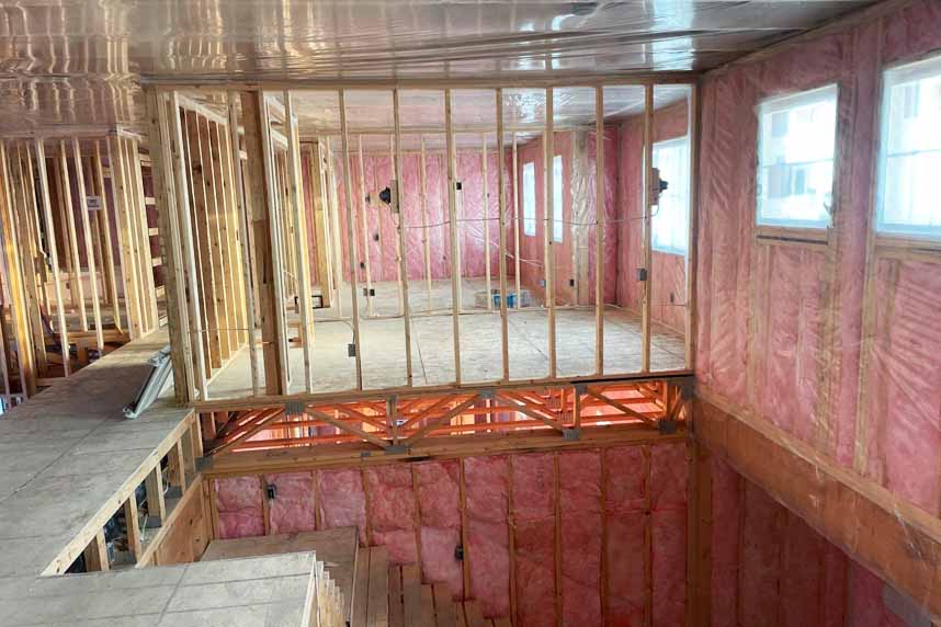 Interior stairwell of a multifamily residential building under construction, with exposed wood framing and pink fiberglass batt insulation installed in walls.