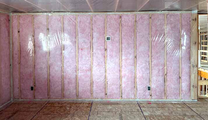 Interior room under construction showing pink fiberglass batt insulation covered by clear polyethylene vapor-barrier sheeting on walls and ceiling framing.